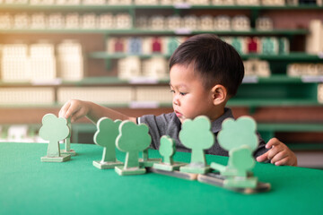 little asian boy is arranging wooden tree block toy on table