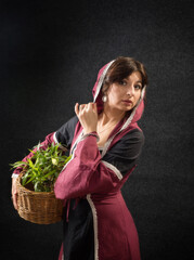 Girl in a medieval dress with a hood and with a basket of greenery. Historical costume.