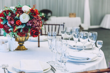 Fancy table set for dinner with flower composition in restaurant, luxury interior background. Wedding elegant banquet decoration and items for food arranged by catering service on white table.
