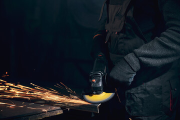 Worker in black gloves working angle grinder with metal.