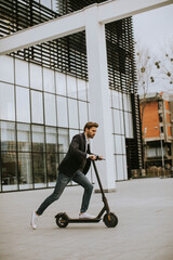 Young business man in a casual clothes riding an electric scooter by an office building on a business meeting