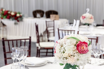 Fancy table set for dinner with flower composition in restaurant, luxury interior background. Wedding elegant banquet decoration and items for food arranged by catering service on white table.