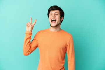 Young Russian man isolated on blue background smiling and showing victory sign