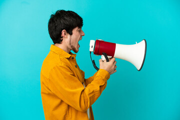 Young Russian man isolated on blue background shouting through a megaphone to announce something in lateral position