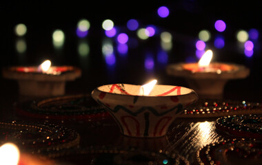 Fototapeta na wymiar Lit up Diwali diyas on a hardwood floor with purple and yellow bokeh
