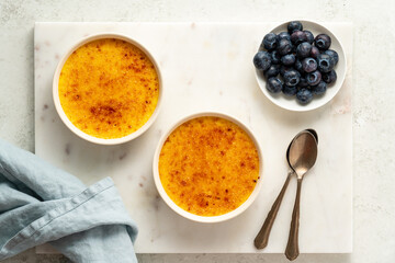 Two ramekin with Creme brulee. Traditional French vanilla cream dessert. Spanish crema catalana, rich custard base. Top view, copy space, marble background