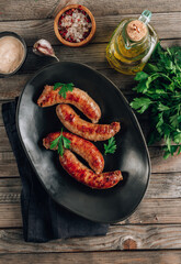 Grilled sausage with greens on black plate over rustic wooden background.