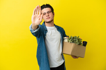 Russian Man making a move while picking up a box full of things isolated on yellow background...