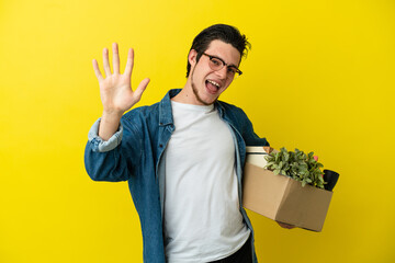 Russian Man making a move while picking up a box full of things isolated on yellow background...