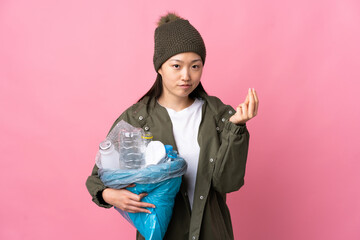 Chinese girl holding a bag full of plastic bottles to recycle over isolated pink background making...