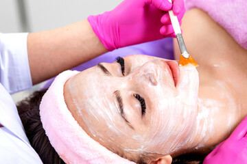 Face peeling mask, spa beauty treatment, skincare. Woman getting facial care by beautician at spa salon, side view, close-up. Anti-aging treatment. Cosmetology and professional facial skin care.