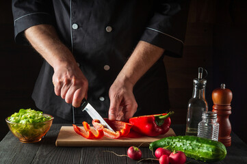 Close-up of a chef hands cutting peppers on cutting board. Professional preparation of salad in the kitchen in a restaurant or cafe