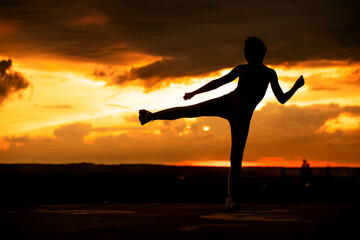 Silhouette of a fitness woman stretching at sunset with the sun in the background