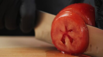Close-up of a chef cutting a red tomato with a knife on a wooden board. Slicing a tomato with a knife. Cutting vegetables - Powered by Adobe