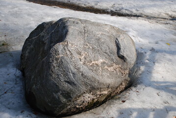 Large boulder stone on the ground surrounded by snow. On the ground lies a large gray granite stone...