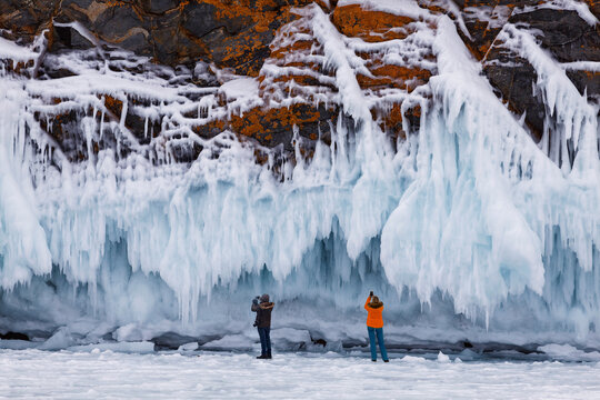 Tourists take pictures of a beautiful landscape with rocks covered with ice on Lake Baikal. South-Eastern Siberia, Russia