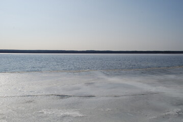 Obraz premium A river is being freed from ice. Spring day light blue sky, river flood with blue water. At the very shore there is a small strip of ice, the middle of the river is without ice. On other side trees