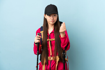 Young Chinese girl with backpack and trekking poles over isolated blue background making Italian gesture