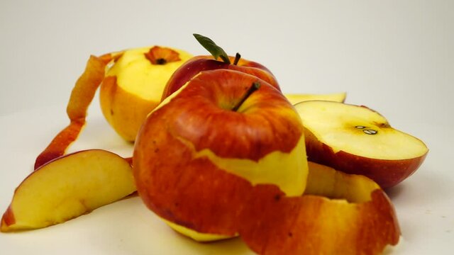 Ripe fresh apples, whole, partially peeled, slices and apple peels lie on a white table, slow motion