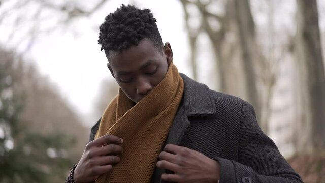 Black man putting scarf outdoors in winter season. African guy adjusting scaf in the cold wearing coat