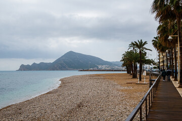 Altea beach, with palm trees, and people walking along a wooden walkway, on a rainy day.