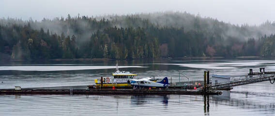 Float plane and tour boat at dock with passenger waiting  on foggy morning, Port Hardy, Vancouver Island, British Columbia, Canada