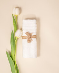 Wellness, spa composition with white towel and tulips on light background. Preparation for relaxation procedure, spa treatment, massage. Spring, eco friendly bathing top view