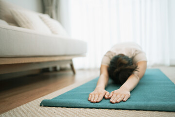 Portrait of gorgeous young asian woman practicing yoga at home stretching out while following a yoga routine.