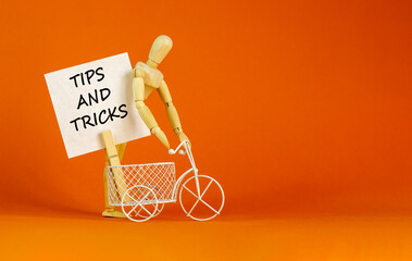 Tips and tricks symbol. White paper. Words 'Tips and tricks'. Miniature bicycle, wooden human. Beautiful orange background. Business and tips and tricks concept, copy space.