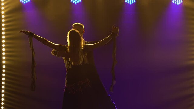 Elements of classical waltz choreography performed by pair of ballroom dancers. Partners man and woman waltz holding hands. Shot in a dark studio against a black background with blue lights. Close up.
