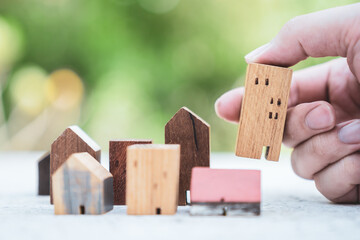 Hand choosing mini wood house model from model on wood table, selective focus, Planning to buy property. Choose what's the best. A symbol for construction ,ecology, loan concepts