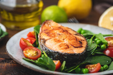 Roasted salmon steak with spinach and tomato salad on a plate, closeup view