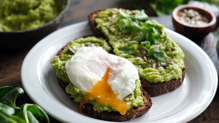 Toast with mashed avocado and poached egg. Rye bread avocado toast with runny egg yolk poached egg cut and mixed seeds