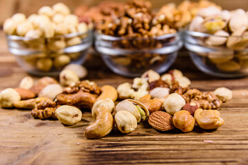 Various nuts (almond, cashew, hazelnut, pistachio, walnut) in glass bowls on a wooden table. Vegetarian meal. Healthy eating concept