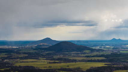 scenic view of Mount Ralsko and Mount Tlustek in the Bohemian Lusatian Mountains as seen from Mount Hochwald in Germany with storm clouds and rain plumes