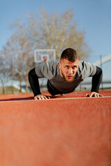 Young fit bearded man doing push-ups outdoors on sunny day. Fitness and sport lifestyle concept.