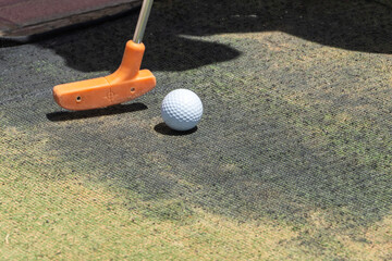 Close up of a minature or mini golf ball and orange putter on artificial grass outdoors with copy space.