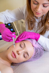 Obraz na płótnie Canvas Beautician makes skin care procedure on a face. Cosmetologist applying a woman a cosmetic medical gel in a face from a syringe. Woman in a spa salon on cosmetic procedures for facial care.
