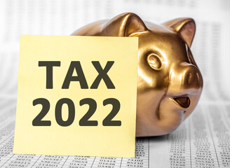 golden pig saving bank and yellow paper for text TAX 2022 on wooden table with many page financial...