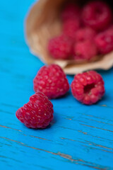 Vertical format of macro photo. Red appetizing raspberres from paper cornet on blue painted background