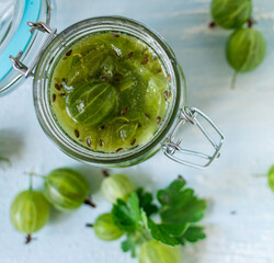 Gooseberry jam in a glass jar and berries scattered around. No-cook jam. Food background. Top view