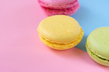 Fototapeta na wymiar French macarons on two colored blue pink background. Yellow, green and pink round biscuits close up