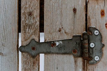 Hand forged iron hinge on the old wooden fence door. Wooden gate with rusty nails and forged loop