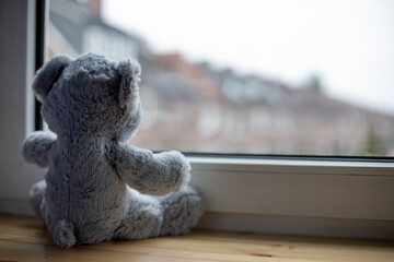 Stuffed animal looking out of a window, symbolizing isolated children during lockdown or quarantine during the corona pandemic