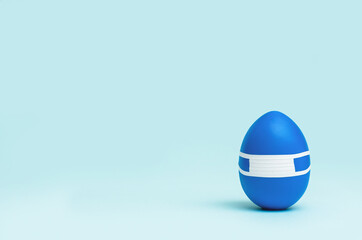 Egg in mask. One blue Easter egg in protective medical mask on blue background. Easter on quarantine concept with copy space.