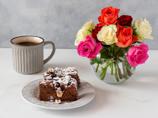 Chocolate nut cake made from buckwheat flour. A mug of coffee and a vase with a bouquet of roses on the table.