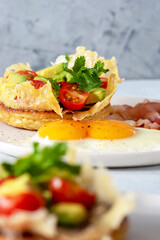 Crumpets are traditional in English-speaking countries lush pancakes made from yeast dough with cheese, avocado and cherry tomatoes. With eggs and fried bacon for breakfast. Selective focus.
