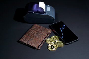 cash register terminal with gold bitcoin coins and wallet on a black background. cash register and coins bitcoin concept. contactless payment with a smartphone, trade and finance.
