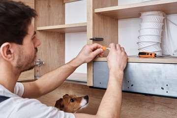 Man fixing wire in kitchen cabinet with dog