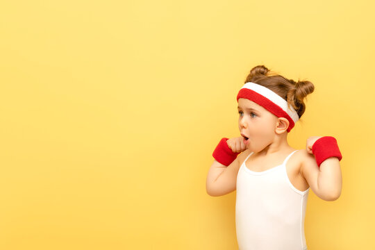 Excited Fitness Child Girl Posing In Sportswear,red Wristbands,headband Over Yellow Studio Background. Children Sport,advertising Concept.Gym Workout.Childhood Activity.Sport.Health And Energy